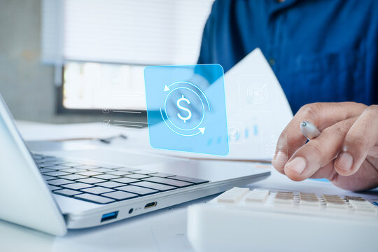 Business professional calculating financial data on desk with laptop and holographic dollar currency exchange icon, concept of corporate finance, investment management, and monetary transactions.