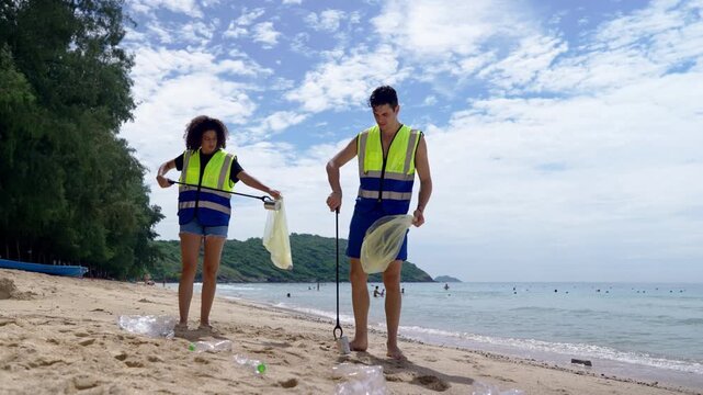 Two volunteers collecting plastic bottles and trash on a sandy beach. 
