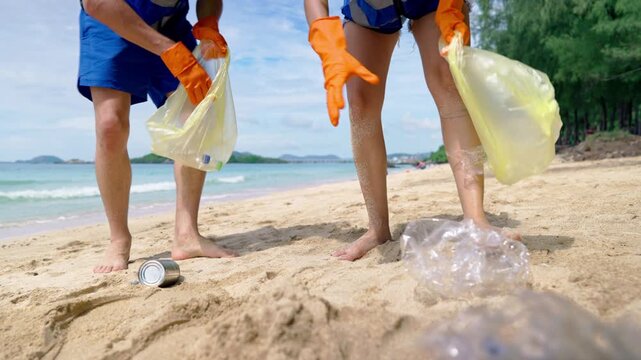 Close up of two volunteers collect plastic bottles and trash on sandy beach.