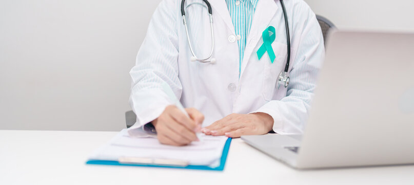 doctor using laptop and report notes on notebook. Teal ribbon concept of September Ovarian Cancer Awareness month, PCOS, January Cervical Cancer, April Sexual Assault, June PSTD, Post Traumatic Stress