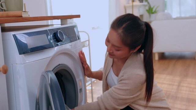 Asian woman laundry washing machine clothing home pink fabric housework, calm young adult sorting clean fabric, loading clothes, folding garment in bright apartment laundry room