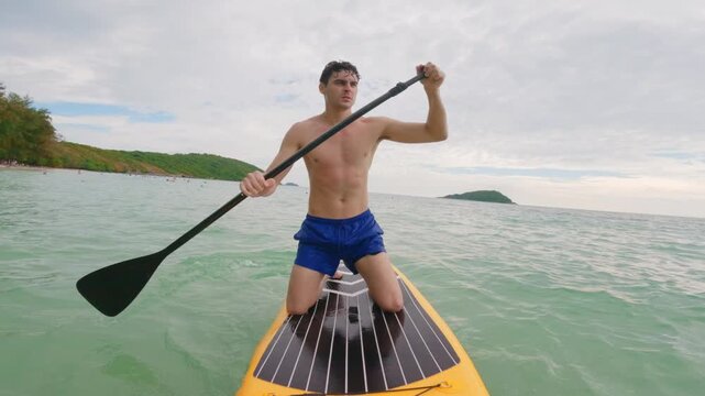 Caucasian young man rows on a paddleboard as glides over the ocean waves. 