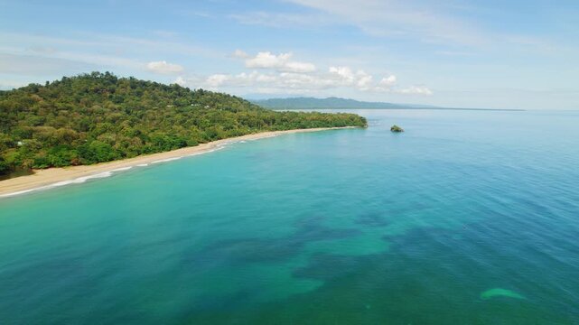 Tropical coastline with green hills meeting calm blue ocean under a clear sky