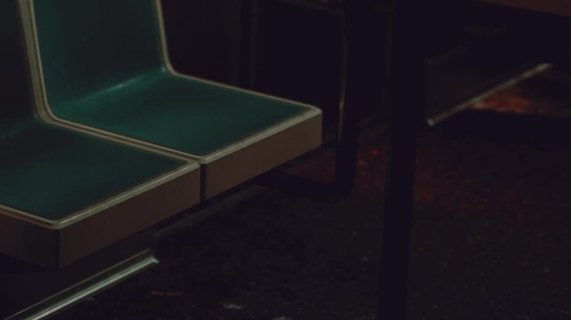Two empty bus seats sit side by side in a dark urban area. The dim lighting highlights the seats, creating a quiet scene. There is no one around and the atmosphere feels still.