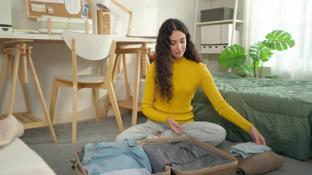 Young Latino woman unpacking clothes and personal items from suitcase. 