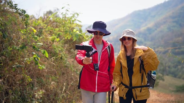 Two hikers use camera record video vlog while walking together on a trail. 