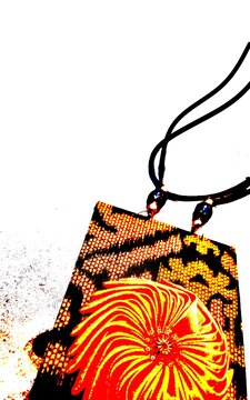 Close-up of a unique handmade ethnic necklace featuring a patterned fabric pendant with a vibrant orange floral design on a black cord. Perfect for fashion, crafts, and cultural accessories.