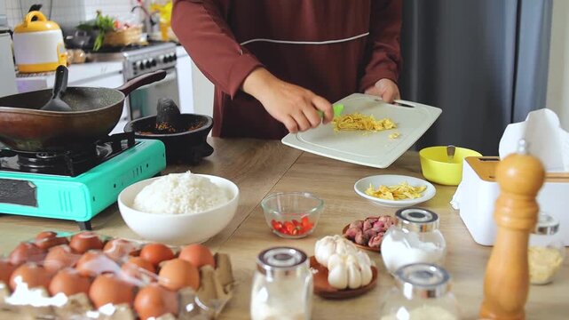 Hands transferring sliced egg omelette strips onto plate in kitchen for fried rice topping