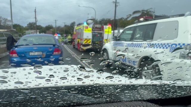 Emergency services including police, fire rescue, and ambulance personnel work swiftly at the scene of a major two-vehicle crash during heavy rain.