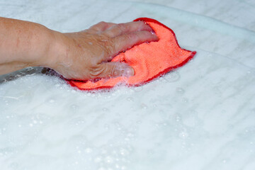 Fototapeta premium Person's hand actively cleaning a dirty surface using a red microfiber cloth and white soap foam, showing household hygiene