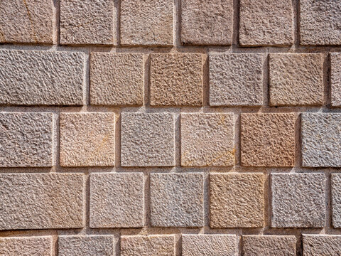 Rough cut stone block wall with geometric masonry pattern, ideal as architectural texture, construction material, facade background, historic building detail and design backdrop.