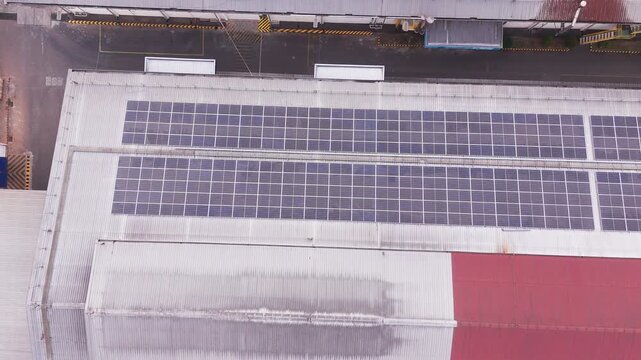 Aerial drone view of a large industrial complex in Indonesia with extensive solar panels installed across factory rooftops. The geometric arrangement of buildings, photovoltaic panels, roads, and surr