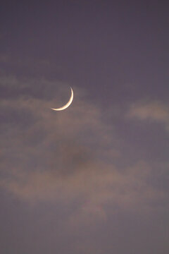 a thin crescent moon shining softly between wispy clouds during twilight