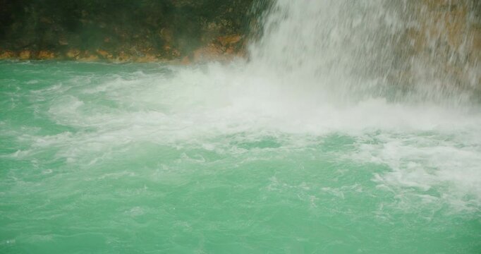 Close view of turquoise water swirling beneath a powerful rainforest waterfall in Costa Rica