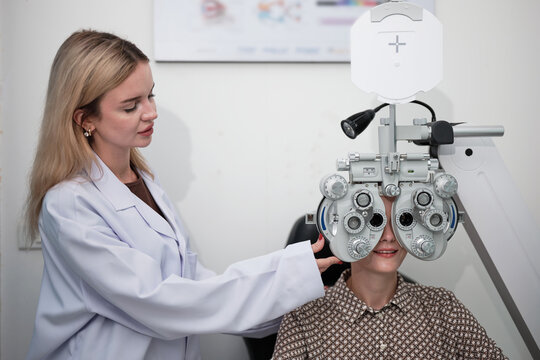 White female patient eye exam with phoropter equipment, vision and eyesight improvement by expert optometrist woman, diagnostic for eyeglasses lens, professional technology services in optical clinic.