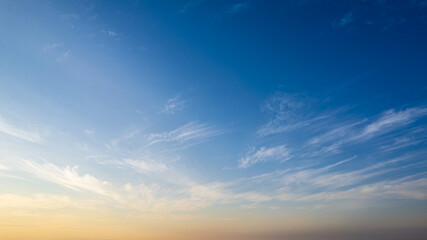 Fototapeta premium Gradient sky from deep blue to warm sunset hues at the horizon, covered in thin, feathery cirrus clouds.