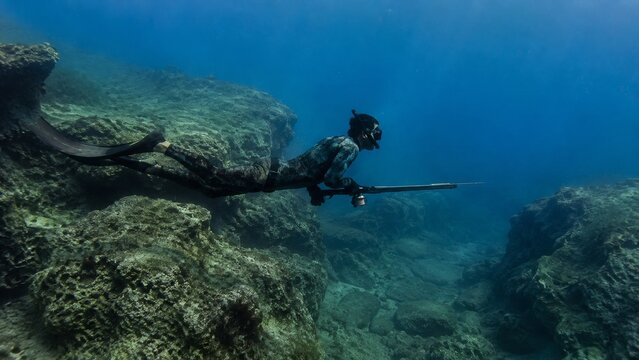 Man holding spear gun diving showing a man gliding over a textured reef with controlled posture