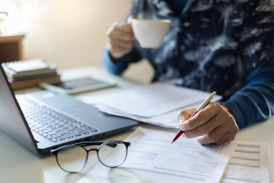 close up shot. asian man in casual clothes working at home checking documents holding coffee cup and using laptop doing online business, start e-commerce business via application online