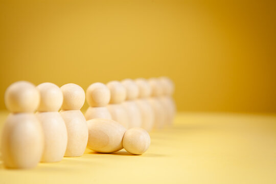 Wooden figures of people stand in a row on a yellow background