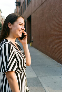 Woman laughing on phone call standing on urban brick wall street