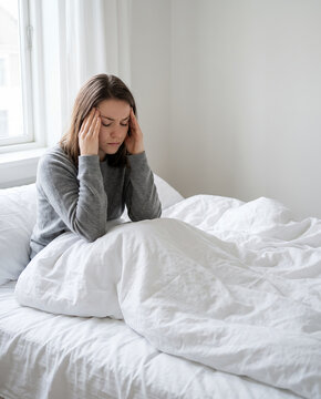 Woman curled up in white bed under covers sunlit bedroom morning