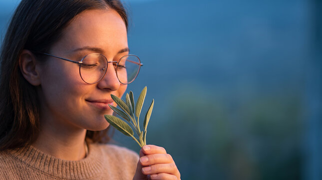 Young woman with eyeglasses admiring olive plant against blue backdrop