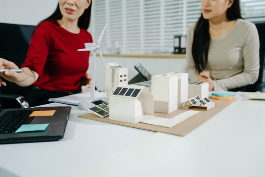 Engineers discuss eco-friendly architecture using green solar panels and wind turbine models for sustainable urban development.