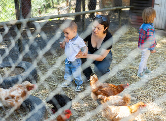 Woman with children near yard with hens, excursion to farm. Mom shows daughter and son livestock, outdoor weekend. © JackF