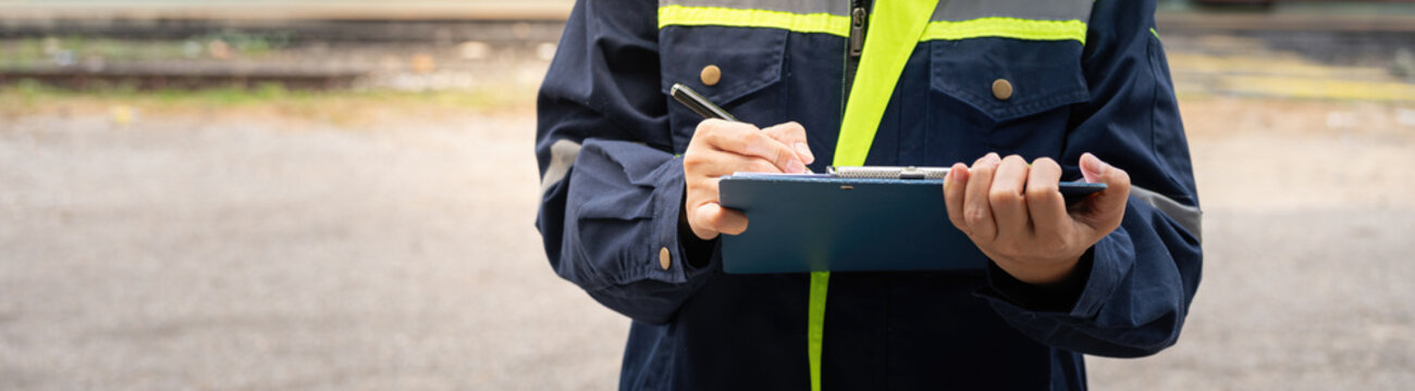 A safety officer is checking on hazardous chemical material checklist for risk assessment before tranportation the dangerous good with train tanker railway background. Industrail working scene.