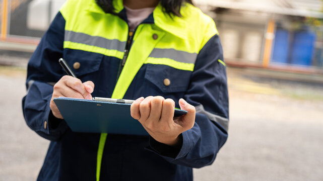 A safety officer is checking on hazardous chemical material checklist for risk assessment before tranportation the dangerous good with train tanker railway background. Industrail working scene.