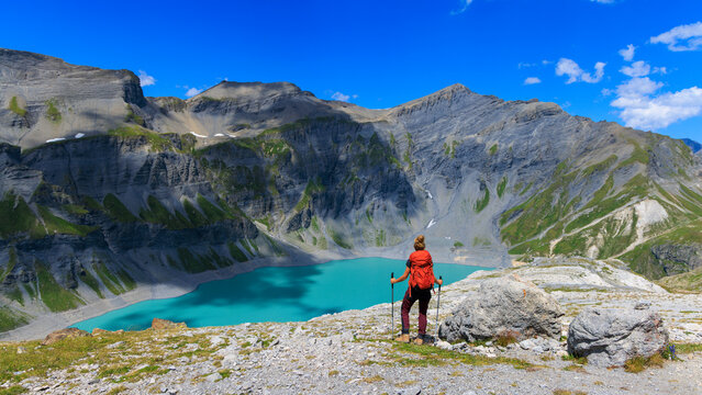 woman hiker with red backpack looking at alpine turquoise lake in mountains, Switzerland, lac du vieux Emosson, Hikes and trail