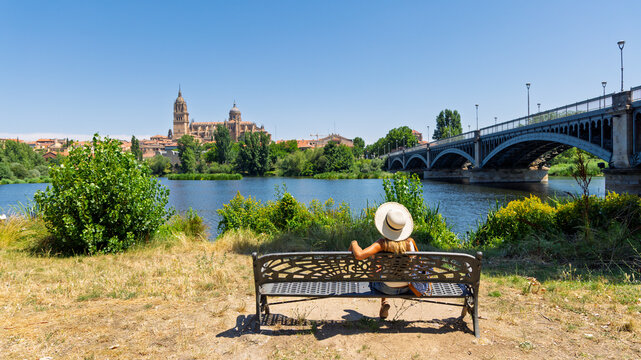 young woman sitting on bench looking at Salamanca cathedral and bridge in Spain