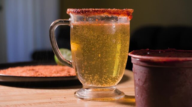 Close up footage of a man adding fresh lime and Tajin seasoning to a beer cup while preparing a savory homemade chamoy michelada drink