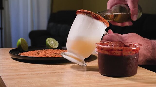Close up footage of a man pouring cold beer into a frosted cup while preparing a savory homemade chamoy michelada drink