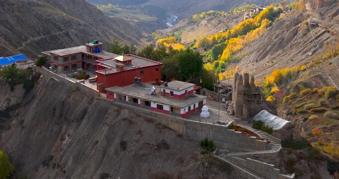 Annapurna Circuit, Mustang, Nepal, Aerial shot of an ancient red Buddhist monastery perched on a dramatic cliff edge overlooking an arid valley filled with autumn trees and Himalayan mountain peaks.