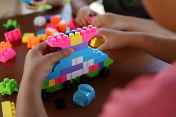 Fotobehang Lego Close up shots of children's hands playing with colorful blocks, building shapes of cars, robots and buildings.  © ArvStd