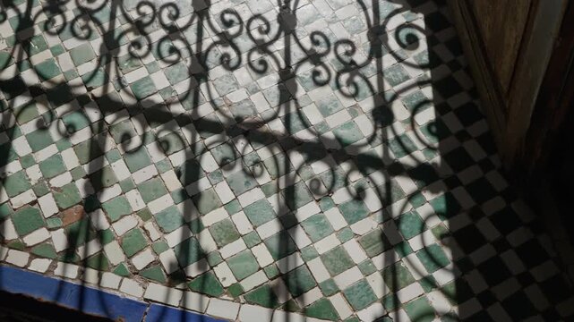 Sunlight casts ornate ironwork shadows on traditional Moroccan tile floor indoors