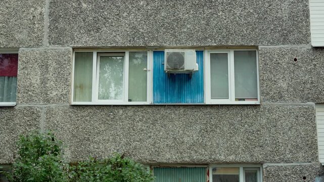 Close up static shot of modern air conditioner unit installed on bright blue panel between apartment windows on textured concrete facade in Daugavpils Latvia.
