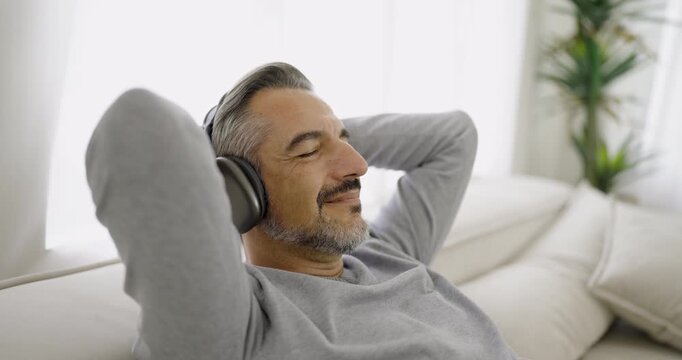 Portrait of senior old caucasian man stay home sit on the sofa living room listen to music head phone. Happy moment of pure love middle age male relax with gadget online digital technology in winter
