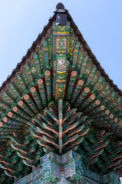 Detailed low-angle view of traditional Korean ornate roof architecture with colorful Dancheong paintings under a blue sky