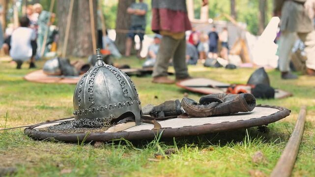 Knights and warriors prepare for a battle as they gather on a grassy area filled with equipment and tools