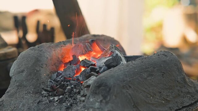 Blacksmiths work with a forge, heating coals to shape iron into tools. The setting shows a traditional workshop with visible tools and materials used in crafting