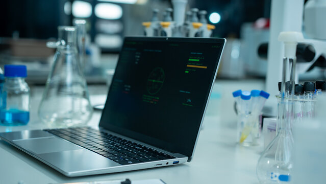 Laptop on a lab desk with glassware and test tubes in a modern science laboratory