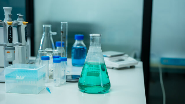 Laboratory bench with glass flasks, pipettes and a green liquid sample for science testing and research.