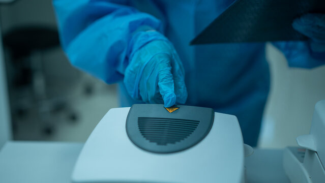 Gloved technician placing a small sample on a laboratory machine in a medical research setting.