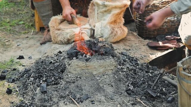 A person prepares to start a fire and shapes tools using a forge in an outdoor setting