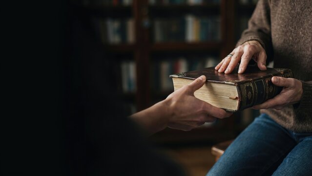 Person handing a thick antique hardcover book to another person