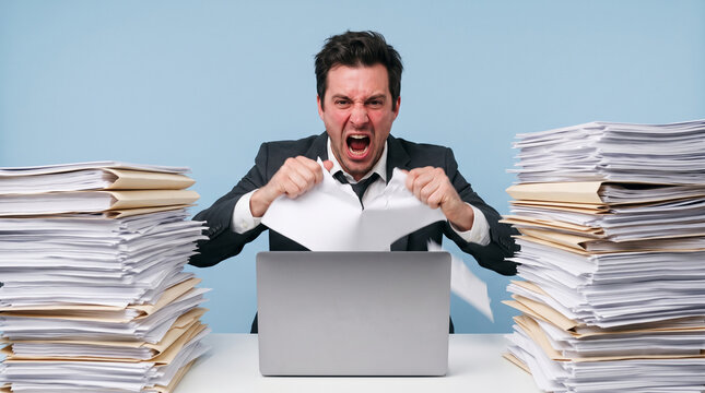 Stressed businessman tearing paper at desk. Overwhelmed employee suffering from burnout.