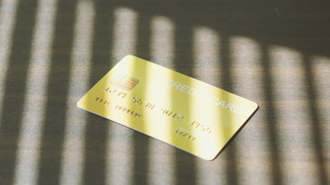 Debt Payment online transaction, gold credit card dropping down on surface with striped window light.