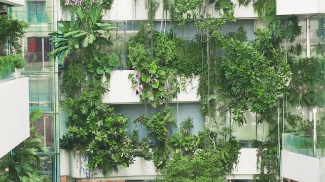 Modern shopping mall facade in Bangkok city with cascading greenery, tropical plants and water flowing down tiered balconies, creating vertical waterfall in dense urban setting